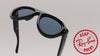 Black Ray-Ban Rock sunglasses with blue lenses, shown at an angle on a light gray background with a red ASAP Ray-Ban Rock logo overlay in the bottom right corner.